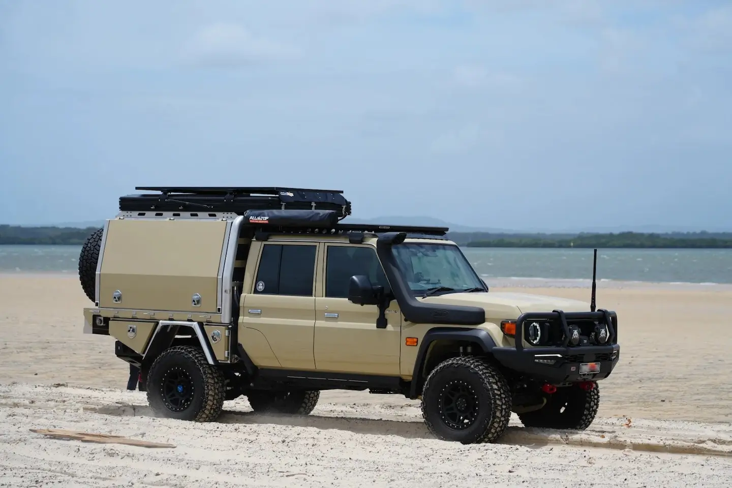 Sand-coloured Land Cruiser 79 double-cab with an aluminium tray canopy on a beach